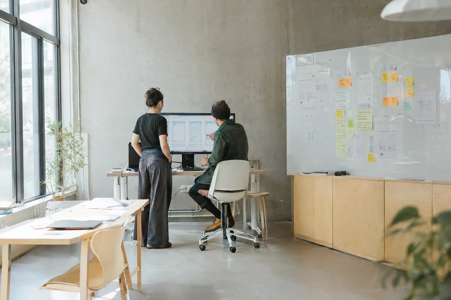 Two designers reviewing interface wireframes on a large monitor in a bright studio